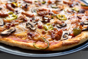 Very close shot of a freshly made green pepper, onion, mushroom, cherry tomato, mozzarella, pepperoni and ham pizza.