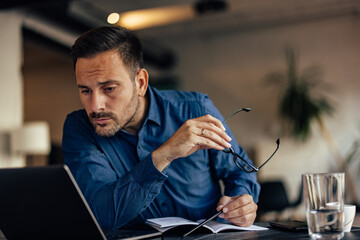 Businessman looking closely to the laptop, reading something online.