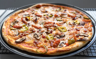 Close up of a freshly made ham and vegetable pizza on a cooling rack in the kitchen at home. Healthy food concept. Cook at home.