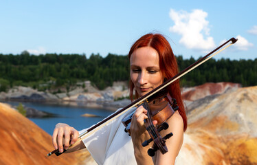 Woman playing a violin in a red sunset in nature quarry with Martian landscapes
