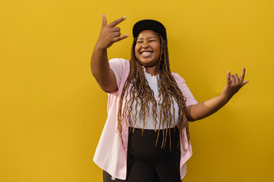 Happy woman showing horn sign gesture in front of yellow wall