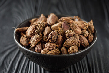 a barrel of dried black cardamom on a black wooden rustic background