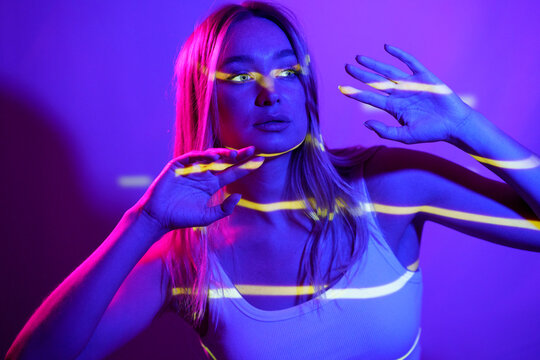 Woman gesturing with neon colored lighting in front of wall