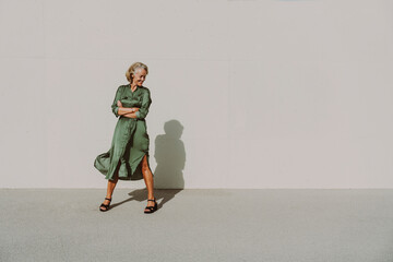 Smiling mature woman with arms crossed in front of white wall