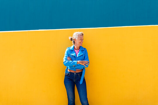 Mature woman with arms crossed leaning on colored wall