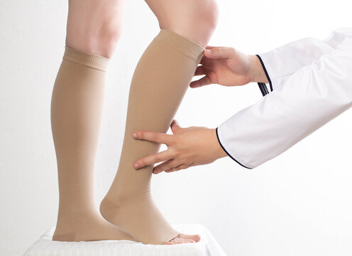 The phlebologist doctor selects the size of the patient's compression stockings. White background, close-up.