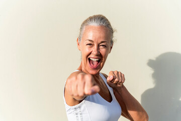 Happy woman showing fists in front of wall on sunny day