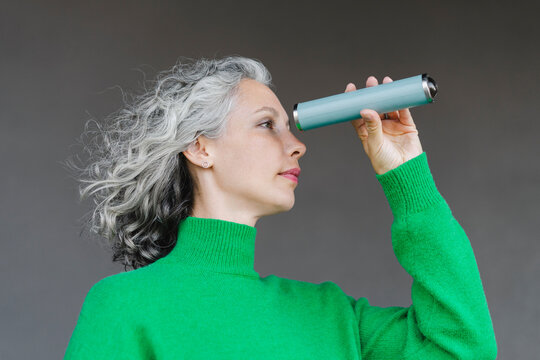 Woman with curly gray hair looking through monocular in front of wall