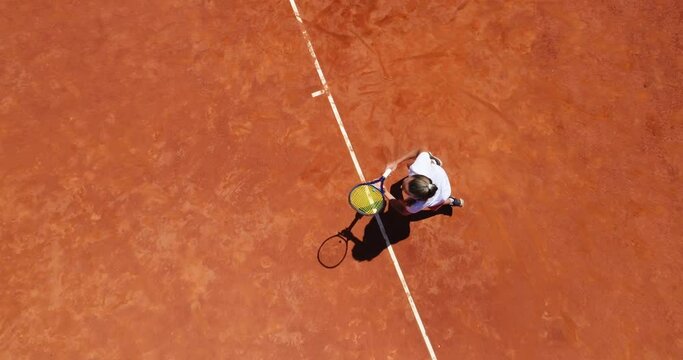 Aerial top view of a young female tennis player playing on brown ground court. Professional girl tennis player hitting a backhand on court Flat layout sport background. 