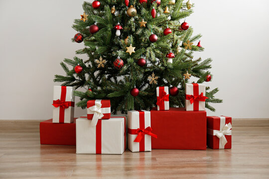 Cropped shot of beautiful christmas tree decorated with shiny baubles and many different presents on wooden floor. White wall background with a lot of copy space for text. Close up.