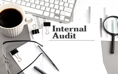 INTERNAL AUDIT text on a paper with magnifier, coffee and keyboard on grey background
