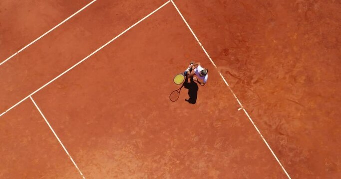 Aerial top view of a young female tennis player playing on brown ground court. Professional girl tennis player hitting a backhand on court Flat layout sport background. 