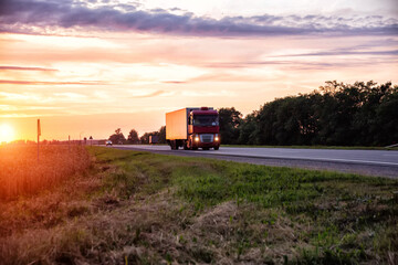 Fototapeta premium A modern truck with a semitrailer refrigerator transports cargo against the backdrop of an evening sunset in summer. Road freight industry. Goods turnover,