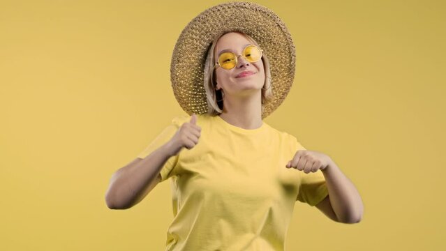 Smiling woman pointing down to advertising area. Yellow background. Young lady asking to click to subscribe below. Copy space for your commercial idea, promotional content.