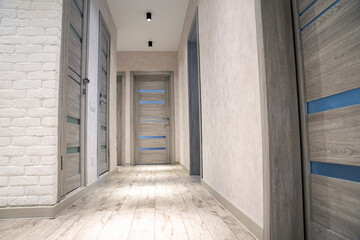 Modern corridor in an apartment after renovation in gray tones. Gray interior doors and black LED lights on the ceiling. white brick wall