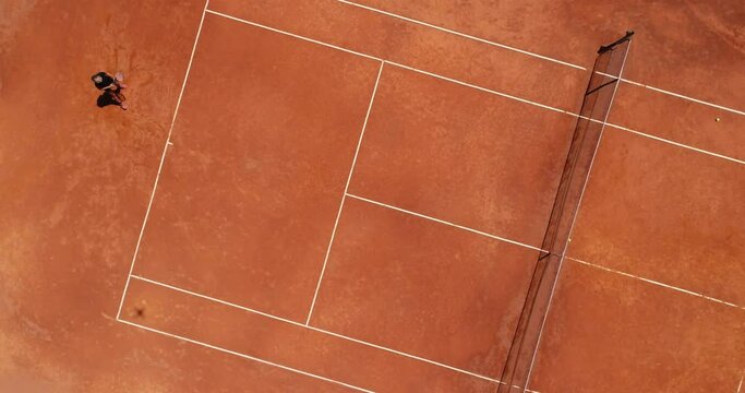 Aerial top view of a young female tennis player playing on brown ground court. Professional girl tennis player hitting a backhand on court Flat layout sport background. 
