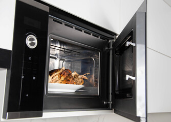 Hot grilled chicken in the microwave in a plate. Heating food in the microwave oven, convection and grill. Modern household kitchen appliances