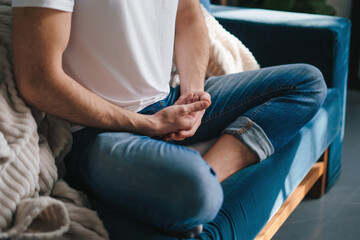 Close-up view of man's legs crossed on sofa and hands crossed in meditation position. Health care. Body care.