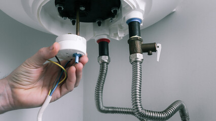 Repair and maintenance of boilers. The hand of a plumber installs a thermostat in a boiler after repair. Water heater repair.