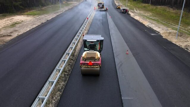 The road roller compacts and levels the new hot asphalt. Steam rises above the tarmac. Pavement technology. The final stage of highway repair. The concept of improvement of the urban environment.