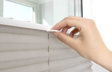 A man opens the blinds on the window to let sunlight into the room. Aluminum classic blinds with scaffold fixing system. Close-up