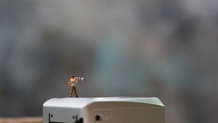 a miniature figure taking picture with a camera against a real camera in the background.