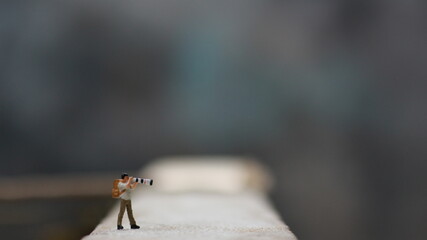 a miniature figure taking picture with a camera against a real camera in the background.