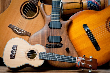 Fototapeta na wymiar Acoustic and electric guitars, ukulele and djembe standing side by side on a wooden background.