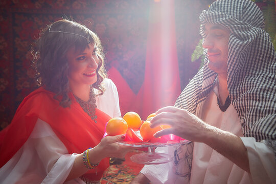 Portrait of young arabian muslim couple in traditional clothes in cozy red room. Fhoto shoot in easten style with male and female model like in a harem with a sultan and an odalisque