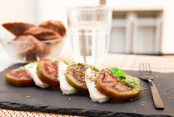 caprese salad with mozzarella, black tomatoes and pesto on black stone plate