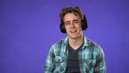 Portrait of dancing, grooving young man 20s wearing headphones, enjoying music. Handsome guy surprised isolated on solid purple background.