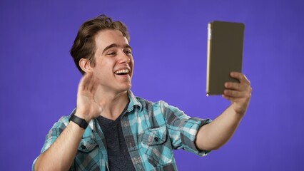 Portrait of happy smiling young guy 20s in shirt having video chat on tablet computer conducting pleasant conversation isolated on purple background studio. 