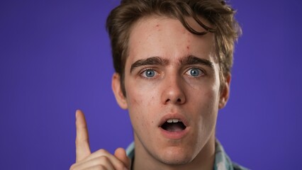 Closeup portrait of thinking, smart puzzled pensive young hipster man 20s thinks comes up with ideas raised finger thumbs up isolated on purple background studio