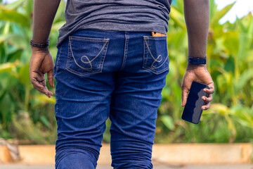 Jeune homme africain tenant un smartphone, présente l'écran de  son téléphone vue d'arrière
