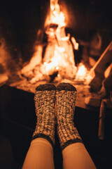 Female feet in warm woolen socks in front of cozy fireplace.
