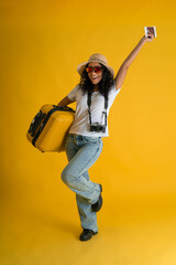 Fototapeta na wymiar Happy Traveller curly latin woman wears white t-shirt with suitcase bag, passport and boarding tickets isolated on yellow background.
