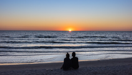 Beach lovers watching the sunset sitting on a sandy beach