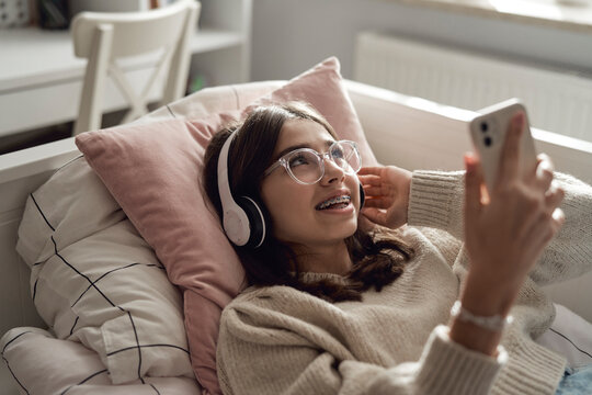 Caucasian teenage girl browsing phone with smile and wearing headphones