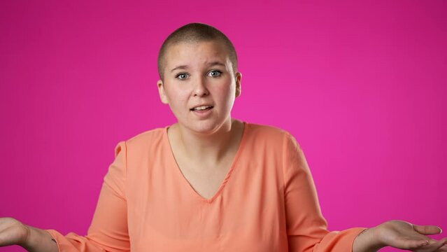 Portrait of happy pretty gender fluid non binary woman 20s shrugging shoulders and gesturing I do not know isolated on pink background.