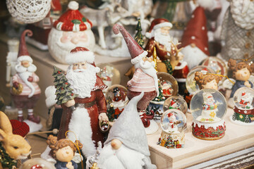 Stylish Christmas souvenirs, santa clauses, snow globes, snowman toys in showcase of festive store....