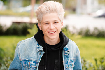 Smiling teenager boy 16-17 year old with short blond hair wear denim jacket and black hoodie...