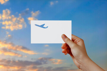 Man's hand holding airplane symbol paper in sky. Concept of journey, travel, dream, freedom. Hand is holding paper airplane against blue sky with empty space for text.