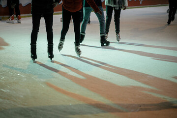 Fototapeta na wymiar Ice skaters on ice rink, skates close up. People having fun and skating in town square in evening.Legs with ice skaters cropped view. Atmospheric Winter holidays in Europe. Happy Holidays!