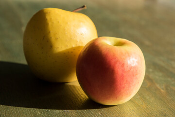 Yellow apples closeup indoor lit by sunlight on green wooden surface