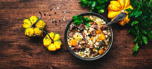 Obraz na płótnie Canvas Autumn food. Warming soup with pumpkin, mushrooms, vegetables, beef and barley. Rustic wood table background, top view banner