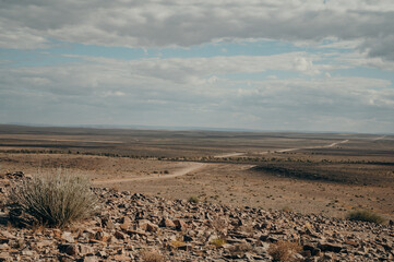 On the Road im Süden Namibias - Blick in Richtung einer einsamen Straße, auf der in der Ferne ein Auto zu erkennen ist (Namibia)