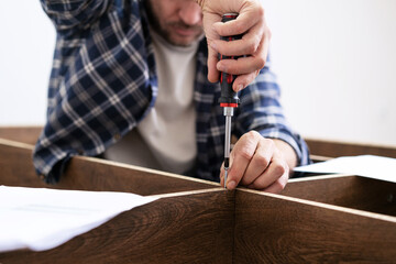 Assemble wooden furniture screwing self-tapping screw with screwdriver.