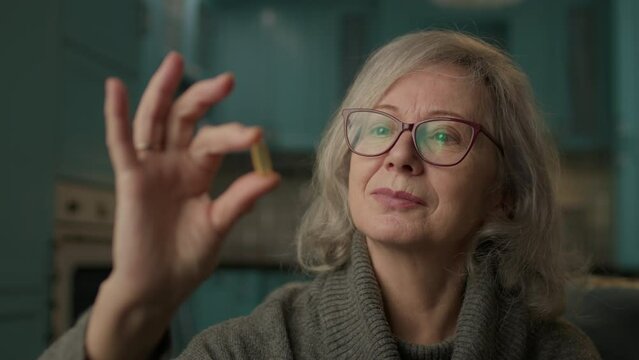 Senior Woman Holding Capsule In Hand. 60s woman taking care of health. Omega-3 fish oil for elderly people is very healthy.