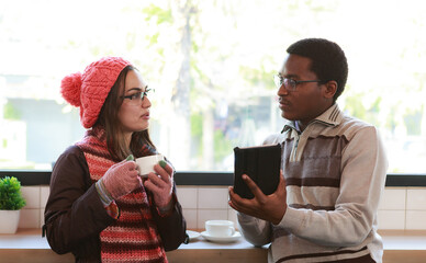 Two young couples in sweaters standing in a cafe smiling and talking. Using tablet. People lifestyle concept. Relax and think while drinking coffee. simulate copy space couple relationship lifestyle
