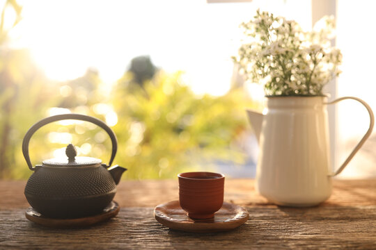 Tea cup and black metal tea pot and flowers on wooden table